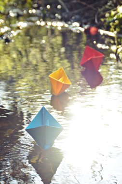 Farklı renkli kağıt gemiler geç sonbahar güneşi yansıtır yüzeyinde küçük bir dere içinde yüzmek-biraz bulanık kağıt gemiler parlak renkler geç sonbaharda bir göl üzerinde