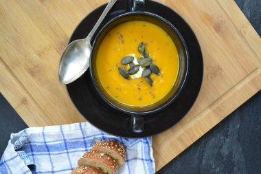 Küçük bir kapta kabak krema çorbası ve yanında bütün bir kabak ve dilimlenmiş ekmek ile mutfak yüzeyinde ahşap bir tahta üzerinde - sonbahar şölen 