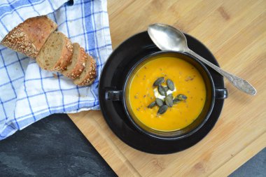 Küçük bir kapta kabak krema çorbası ve yanında bütün bir kabak ve dilimlenmiş ekmek ile mutfak yüzeyinde ahşap bir tahta üzerinde - sonbahar şölen 