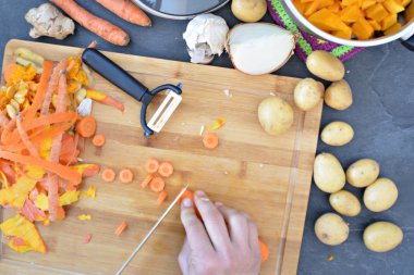 Havuç, patates, soğan, sarımsak ve ahşap bir tahta üzerinde kabak çorbası için bir kabak için sebze kesme ve yukarıda elleri üzerinde pot-closeup içine dökme 