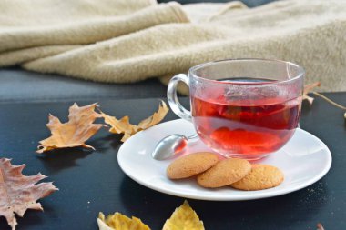 Karanlık bir arka planda çay ile otomatik ayar-bir cam fincan yüzen meyve çayı bir teabag, yanında kurabiye ve kurutulmuş sonbahar yaprakları