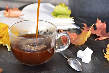 Bir cam fincan içine bir sonbahar ayarı kahve dökün-bir cam fincan kuru ve renkli sonbahar yaprakları ve arka planda bir kitap yanında standig ve birisi içine kahve dökme olduğunu