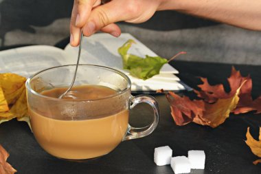 Bir cam fincan içine bir sonbahar ayarı kahve dökün-bir cam fincan kuru ve renkli sonbahar yaprakları ve arka planda bir kitap yanında standig ve birisi içine kahve dökme olduğunu