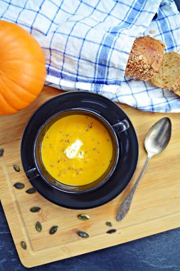 Küçük bir kapta kabak krema çorbası ve yanında bütün bir kabak ve dilimlenmiş ekmek ile mutfak yüzeyinde ahşap bir tahta üzerinde - sonbahar şölen 
