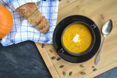 Küçük bir kapta kabak krema çorbası ve yanında bütün bir kabak ve dilimlenmiş ekmek ile mutfak yüzeyinde ahşap bir tahta üzerinde - sonbahar şölen 