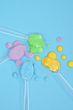 Düz bir arka planda boya farklı damla ile şeffaf kaşıklar-metin alanı ile arka plan olarak renk ile plastik kaşık 