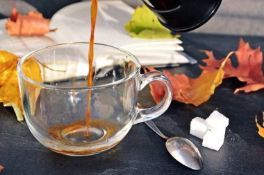 Bir cam fincan içine bir sonbahar ayarı kahve dökün-bir cam fincan kuru ve renkli sonbahar yaprakları ve arka planda bir kitap yanında standig ve birisi içine kahve dökme olduğunu