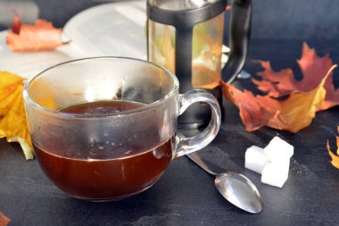 Bir cam fincan içine bir sonbahar ayarı kahve dökün-bir cam fincan kuru ve renkli sonbahar yaprakları ve arka planda bir kitap yanında standig ve birisi içine kahve dökme olduğunu