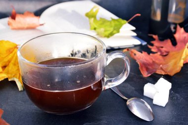 Bir cam fincan içine bir sonbahar ayarı kahve dökün-bir cam fincan kuru ve renkli sonbahar yaprakları ve arka planda bir kitap yanında standig ve birisi içine kahve dökme olduğunu