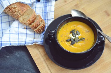Küçük bir kapta kabak krema çorbası ve yanında bütün bir kabak ve dilimlenmiş ekmek ile mutfak yüzeyinde ahşap bir tahta üzerinde - sonbahar şölen 
