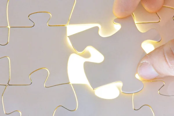 Close-up of a hand putting a white puzzle piece in a total puzzle. The surface of the missing part shines brightly - Concept for the presentation of the radiant success of a completed project