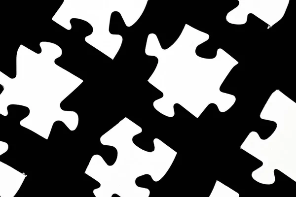 White puzzle pieces against a black background with a certain distance between the individual parts - concept for sub-steps or sub-elements of a large whole presented with puzzle pieces