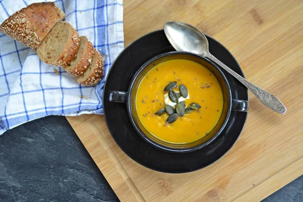 Küçük bir kapta kabak krema çorbası ve yanında bütün bir kabak ve dilimlenmiş ekmek ile mutfak yüzeyinde ahşap bir tahta üzerinde - sonbahar şölen 