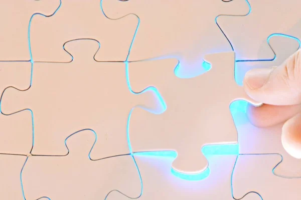 Close-up of a hand putting a white puzzle piece in a total puzzle. The surface of the missing part shines brightly - Concept for the presentation of the radiant success of a completed project