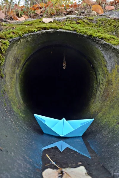 A self-folded paper boat floats in a puddle in nature and is greeted by a pink umbrella with white dots - autumn scenario with paper boat in nature