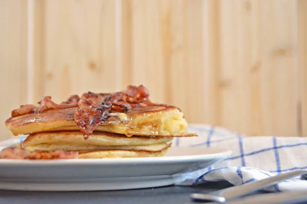 Pancakes with bananas and chocolate sauce on a black table with a wooden background, together with fruit, eggs and a blue white checked kitchen towel