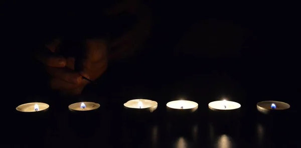 light up a row of candles in the dark with a match - light up candle in a cold evening with focus on the candle and low lightning