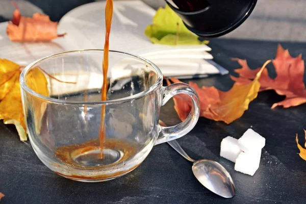 Bir cam fincan içine bir sonbahar ayarı kahve dökün-bir cam fincan kuru ve renkli sonbahar yaprakları ve arka planda bir kitap yanında standig ve birisi içine kahve dökme olduğunu