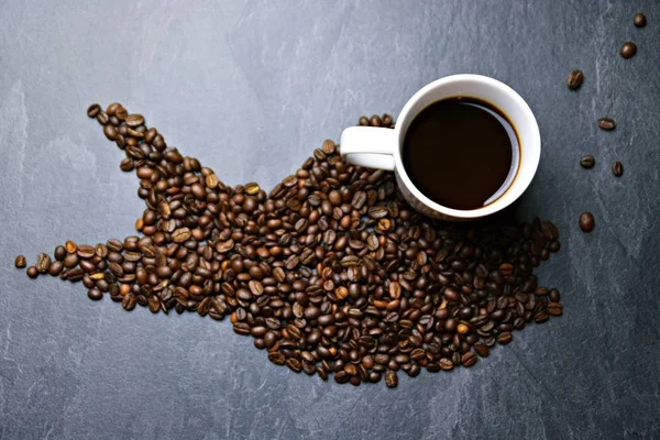 Coffee beans on a black background form the silhouette of a whale and two cups of coffee form their eyes - concept with coffee and whale