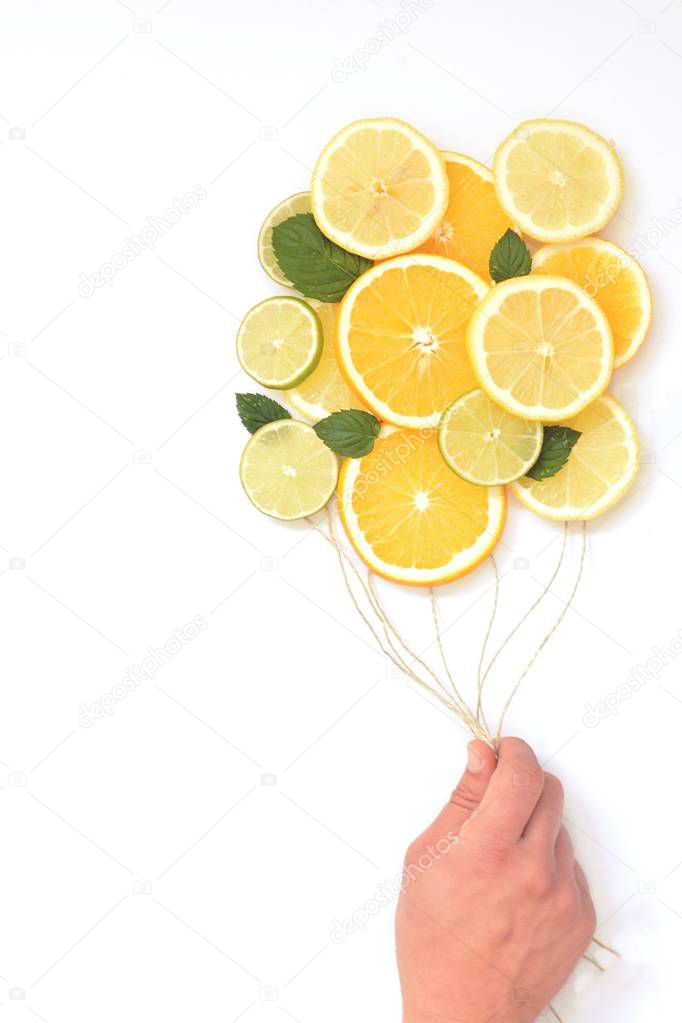 close-up - man holds cords in hand where slices of lemons, limes and oranges are hanging - concept with citrus balloons hovering in front of a monochrome background with space for text