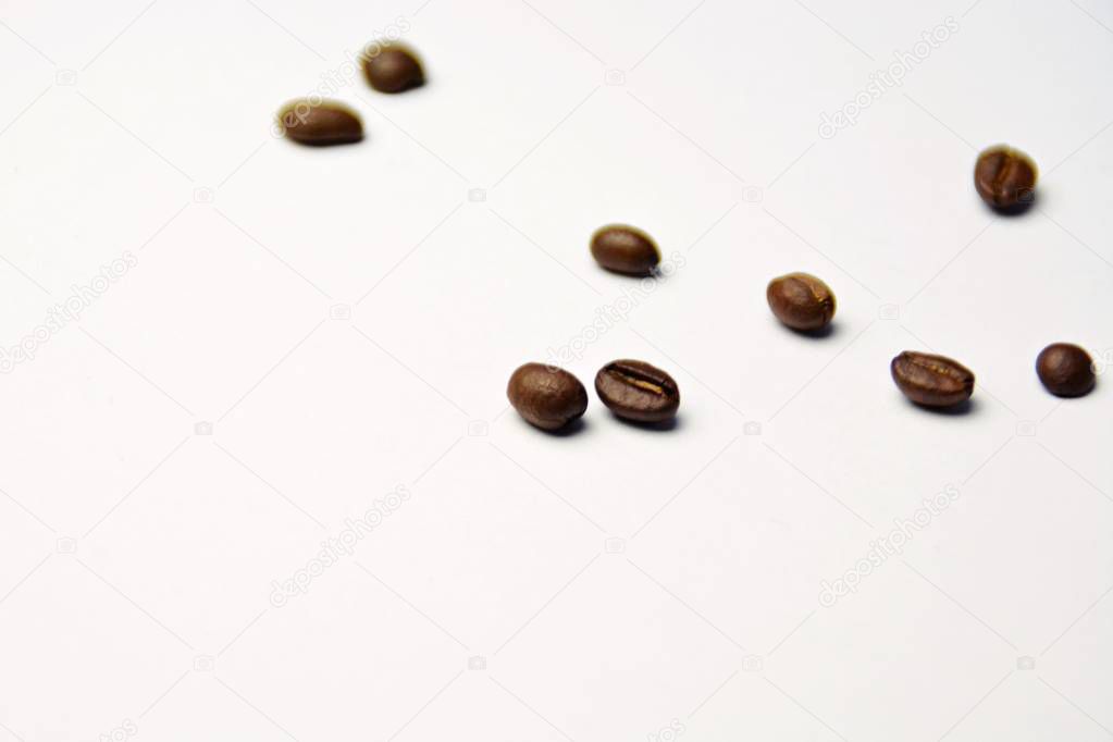 Coffee beans lie on a white surface and protrude into the picture - white background with coffee beans on it and space for text or other elements 