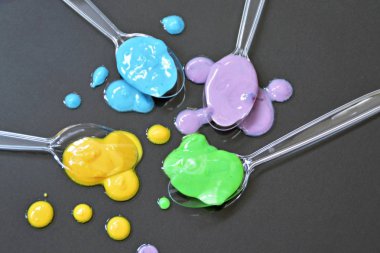 Düz bir arka planda boya farklı damla ile şeffaf kaşıklar-metin alanı ile arka plan olarak renk ile plastik kaşık 