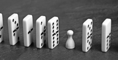 A white wooden pawn stands between lined up dominoes and prevents the vicious circle or the chain reaction from continuing - concept with dominoes and playing figures as creative support  clipart