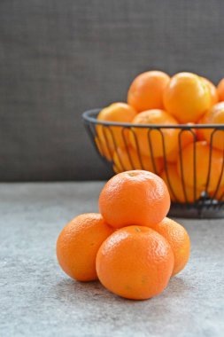 Dört mandalina yığını arka planda mandalina bir sepet ve koyu gri arka plan ile bir mermer plaka üzerinde oturur