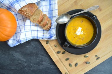 Küçük bir kapta kabak krema çorbası ve yanında bütün bir kabak ve dilimlenmiş ekmek ile mutfak yüzeyinde ahşap bir tahta üzerinde - sonbahar şölen 