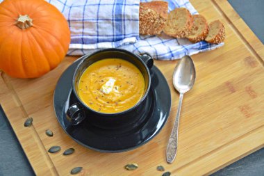 Küçük bir kapta kabak krema çorbası ve yanında bütün bir kabak ve dilimlenmiş ekmek ile mutfak yüzeyinde ahşap bir tahta üzerinde - sonbahar şölen 