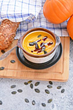 Küçük bir kapta kabak krema çorbası ve yanında bütün bir kabak ve dilimlenmiş ekmek ile mutfak yüzeyinde ahşap bir tahta üzerinde - sonbahar şölen 