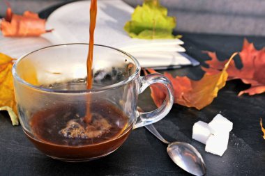 Bir cam fincan içine bir sonbahar ayarı kahve dökün-bir cam fincan kuru ve renkli sonbahar yaprakları ve arka planda bir kitap yanında standig ve birisi içine kahve dökme olduğunu