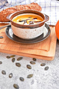 Küçük bir kapta kabak krema çorbası ve yanında bütün bir kabak ve dilimlenmiş ekmek ile mutfak yüzeyinde ahşap bir tahta üzerinde - sonbahar şölen 