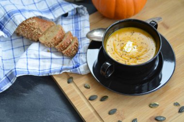 Küçük bir kapta kabak krema çorbası ve yanında bütün bir kabak ve dilimlenmiş ekmek ile mutfak yüzeyinde ahşap bir tahta üzerinde - sonbahar şölen 