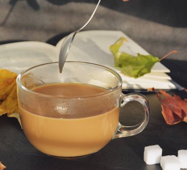 Bir cam fincan içine bir sonbahar ayarı kahve dökün-bir cam fincan kuru ve renkli sonbahar yaprakları ve arka planda bir kitap yanında standig ve birisi içine kahve dökme olduğunu