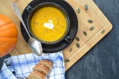 Küçük bir kapta kabak krema çorbası ve yanında bütün bir kabak ve dilimlenmiş ekmek ile mutfak yüzeyinde ahşap bir tahta üzerinde - sonbahar şölen 