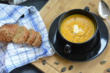 Küçük bir kapta kabak krema çorbası ve yanında bütün bir kabak ve dilimlenmiş ekmek ile mutfak yüzeyinde ahşap bir tahta üzerinde - sonbahar şölen 