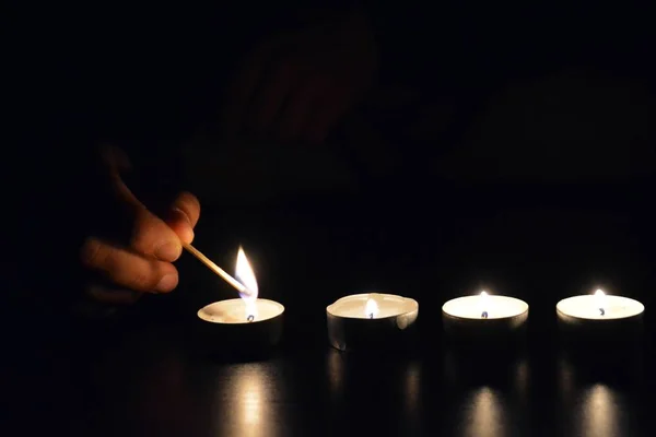 light up a row of candles in the dark with a match - light up candle in a cold evening with focus on the candle and low lightning