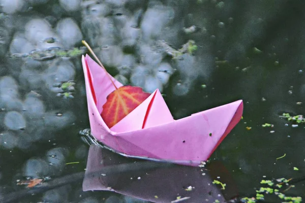 A self-folded paper boat floats on the ground in autumn in a puddle accumulated by the rain