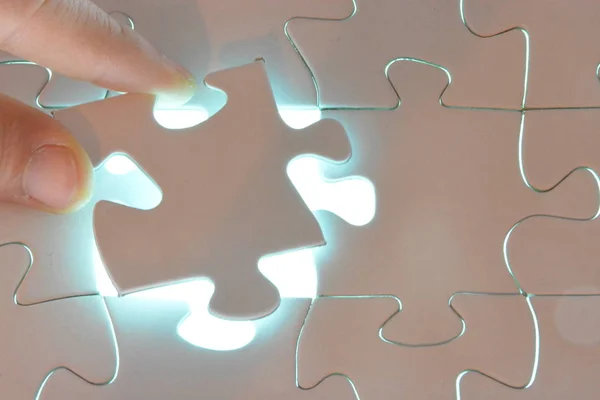 Close-up of a hand putting a white puzzle piece in a total puzzle. The surface of the missing part shines brightly - Concept for the presentation of the radiant success of a completed project