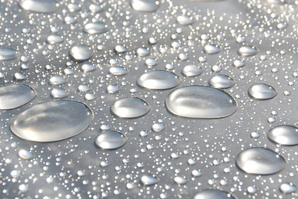 Drops of water collect on a plastic wrap after a rain and reflect the sun shining after the rain - a natural play with light, raindrops and the sun