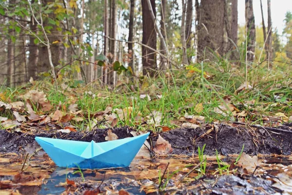 A self-folded paper boat floats in a puddle in nature and is greeted by a pink umbrella with white dots - autumn scenario with paper boat in nature