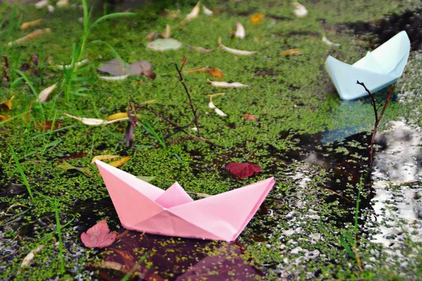 A self-folded paper boat floats on the ground in autumn in a puddle accumulated by the rain