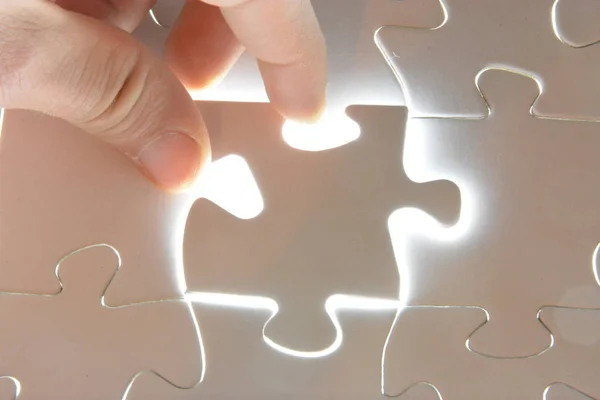 Close-up of a hand putting a white puzzle piece in a total puzzle. The surface of the missing part shines brightly - Concept for the presentation of the radiant success of a completed project