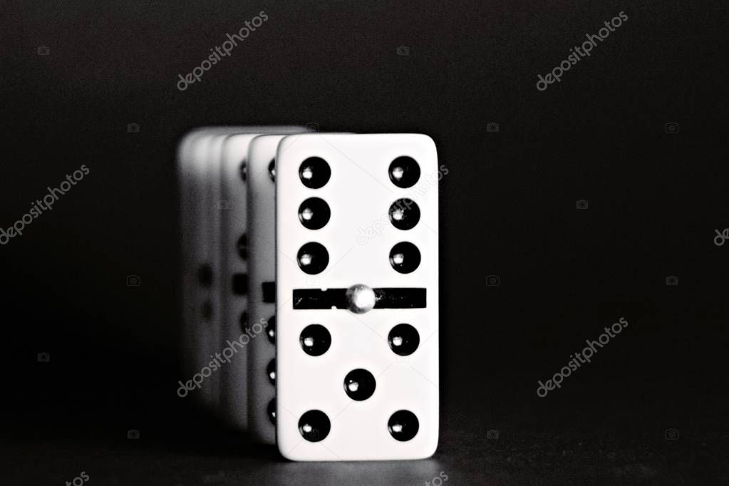 Bright dominoes against a black background with shallow depth of field as a concept for business concepts and subsequent reactions of individual decisions and individual actions 