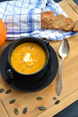 Küçük bir kapta kabak krema çorbası ve yanında bütün bir kabak ve dilimlenmiş ekmek ile mutfak yüzeyinde ahşap bir tahta üzerinde - sonbahar şölen 