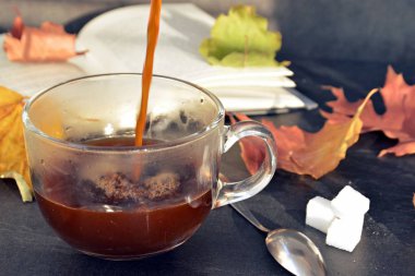 Bir cam fincan içine bir sonbahar ayarı kahve dökün-bir cam fincan kuru ve renkli sonbahar yaprakları ve arka planda bir kitap yanında standig ve birisi içine kahve dökme olduğunu