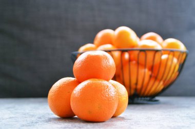 Dört mandalina yığını arka planda mandalina bir sepet ve koyu gri arka plan ile bir mermer plaka üzerinde oturur