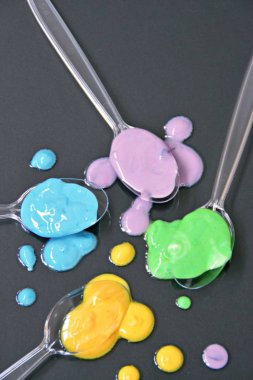 Düz bir arka planda boya farklı damla ile şeffaf kaşıklar-metin alanı ile arka plan olarak renk ile plastik kaşık 