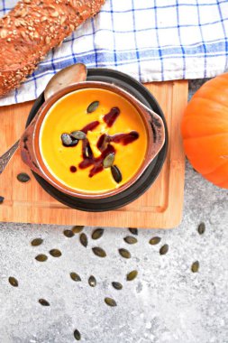 Küçük bir kapta kabak krema çorbası ve yanında bütün bir kabak ve dilimlenmiş ekmek ile mutfak yüzeyinde ahşap bir tahta üzerinde - sonbahar şölen 